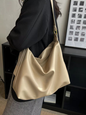 Beige handbag held by a person in a room with a black cabinet and framed pictures.