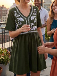 Woman wearing a green dress with white embroidery standing on a rooftop with friends.