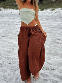 Person wearing a white top and brown pants standing on a sandy beach.