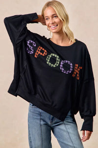 Woman wearing a black sweater with colorful 'SPOOK' text on a beige background