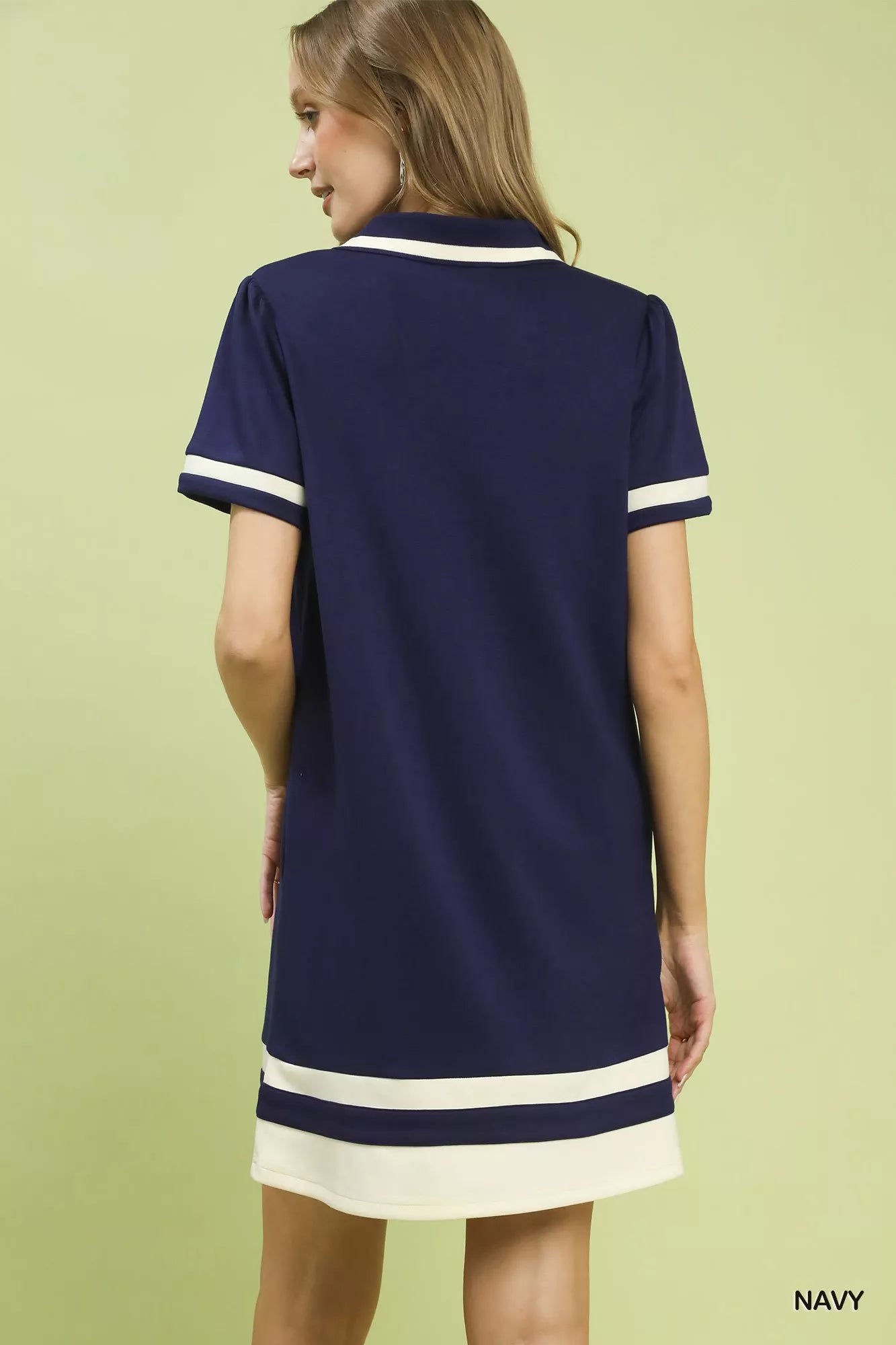 Woman wearing a navy dress with white trim on a light green background