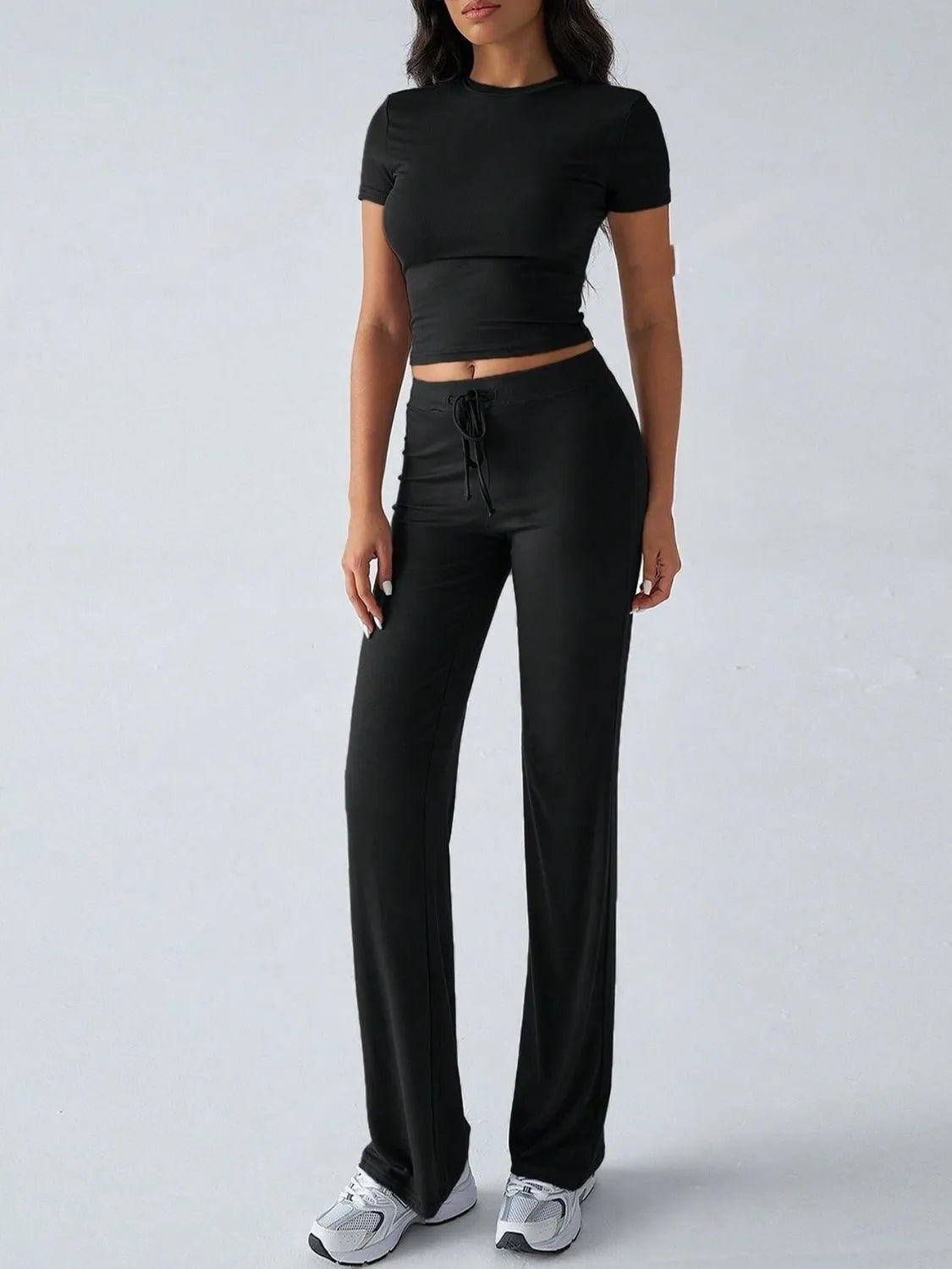 Person wearing a black outfit with a crop top and wide-leg pants on a white background