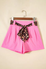 Pink shorts with a leopard print belt on a hanger against a beige background