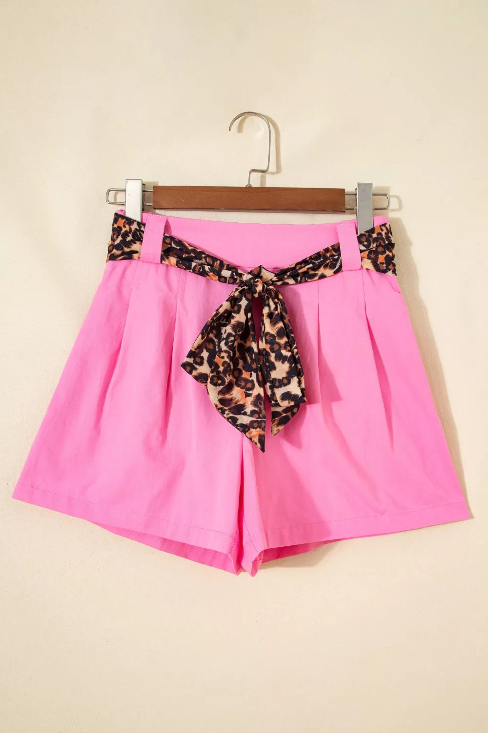 Pink shorts with a leopard print belt on a hanger against a beige background