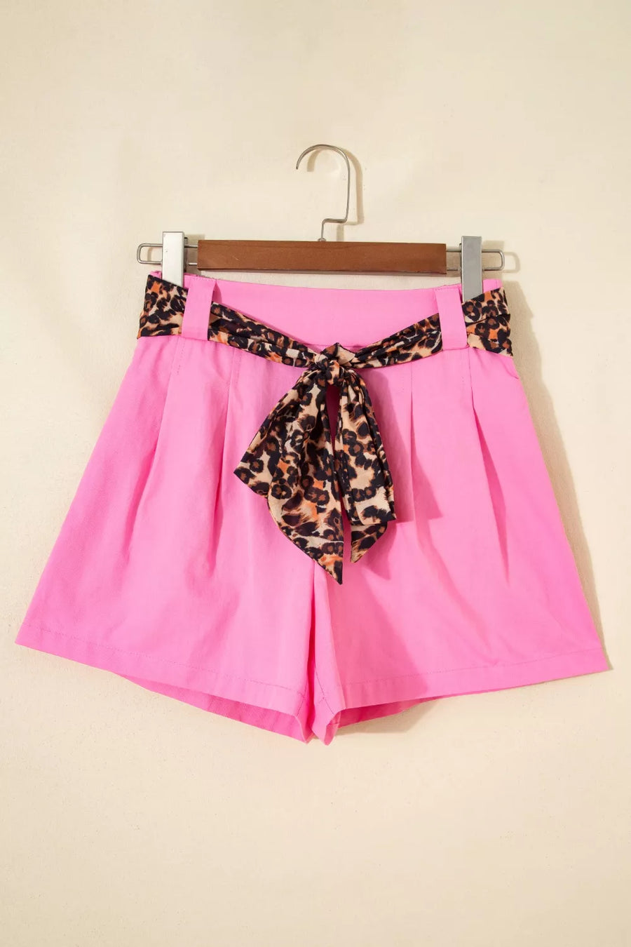 Pink shorts with a leopard print belt on a hanger against a beige background