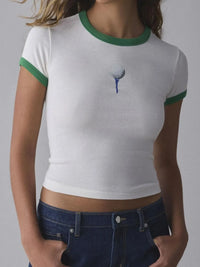 White t-shirt with green trim and golf ball design worn by a person on a gray background