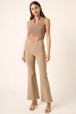 Woman wearing a beige sleeveless top and flared pants on a white background