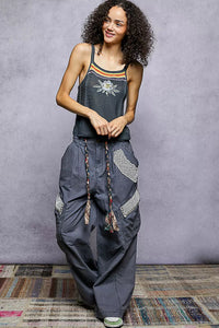 Woman wearing a sleeveless top and wide-leg pants against a gray wall.