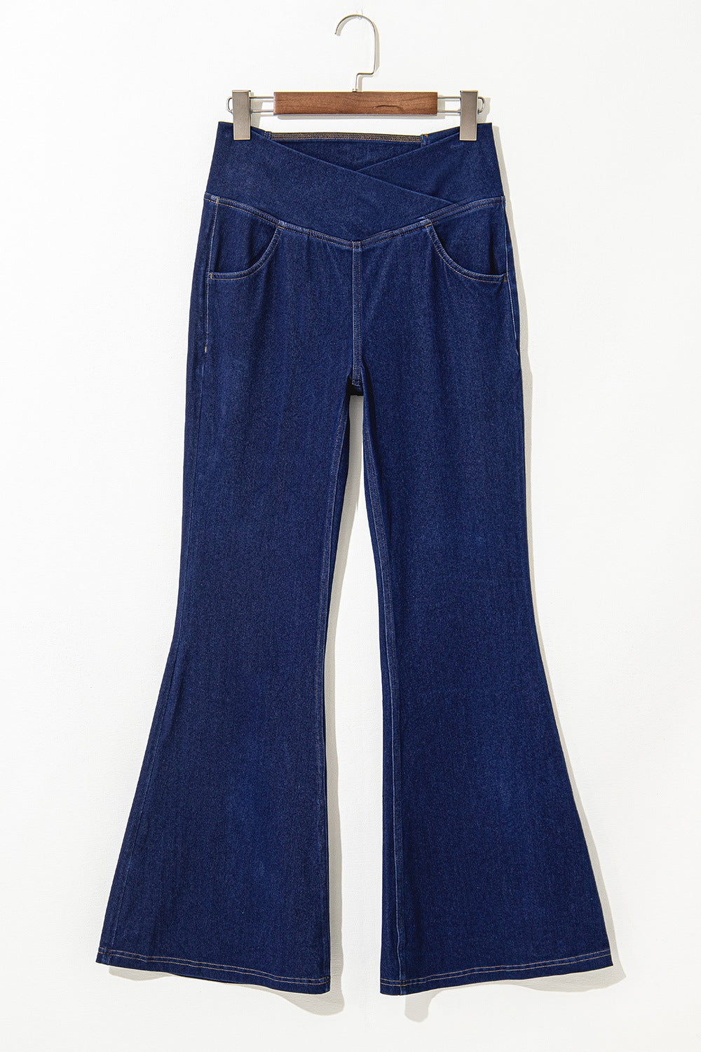 Blue denim bell-bottom pants on a hanger against a white background