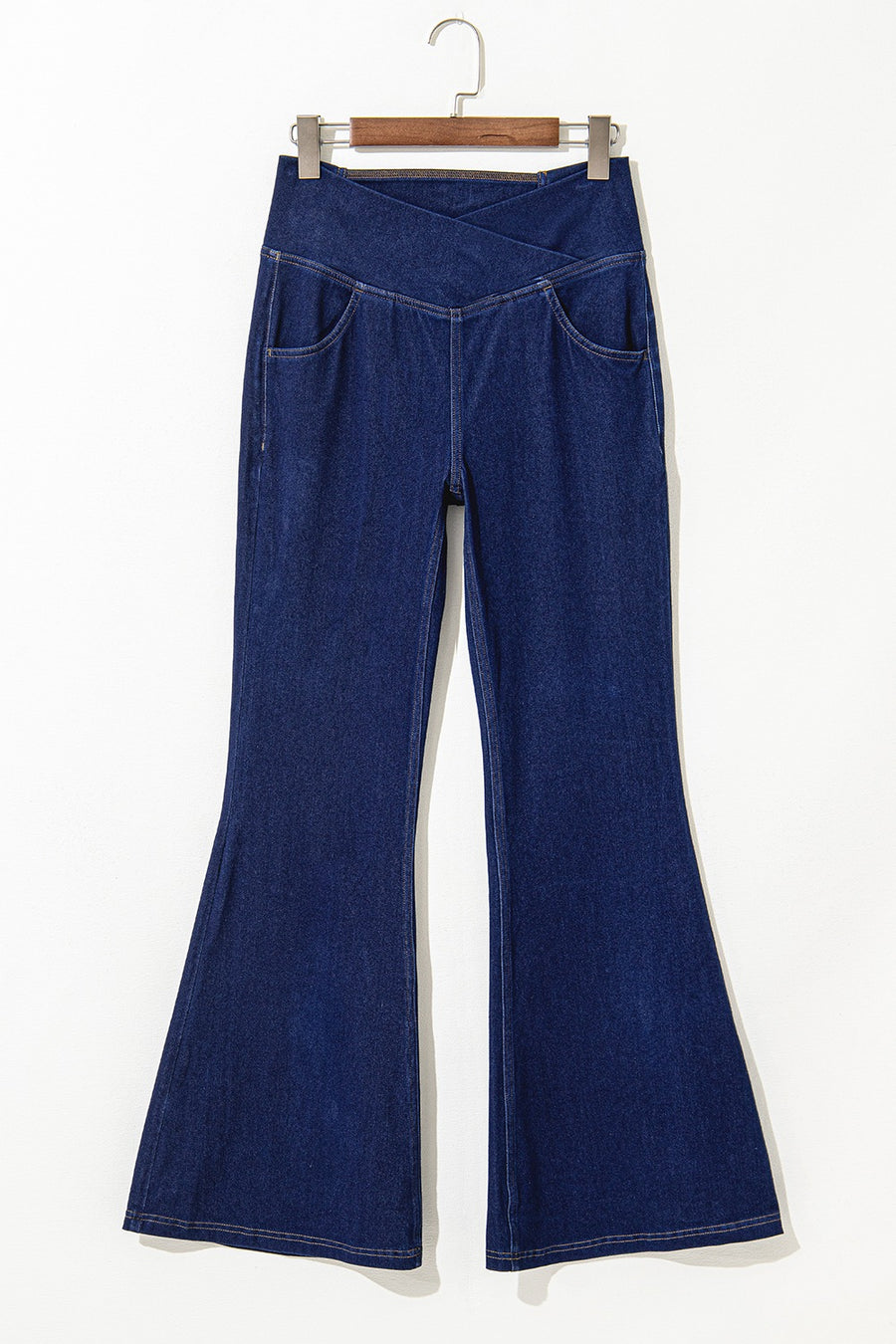 Blue denim bell-bottom pants on a hanger against a white background