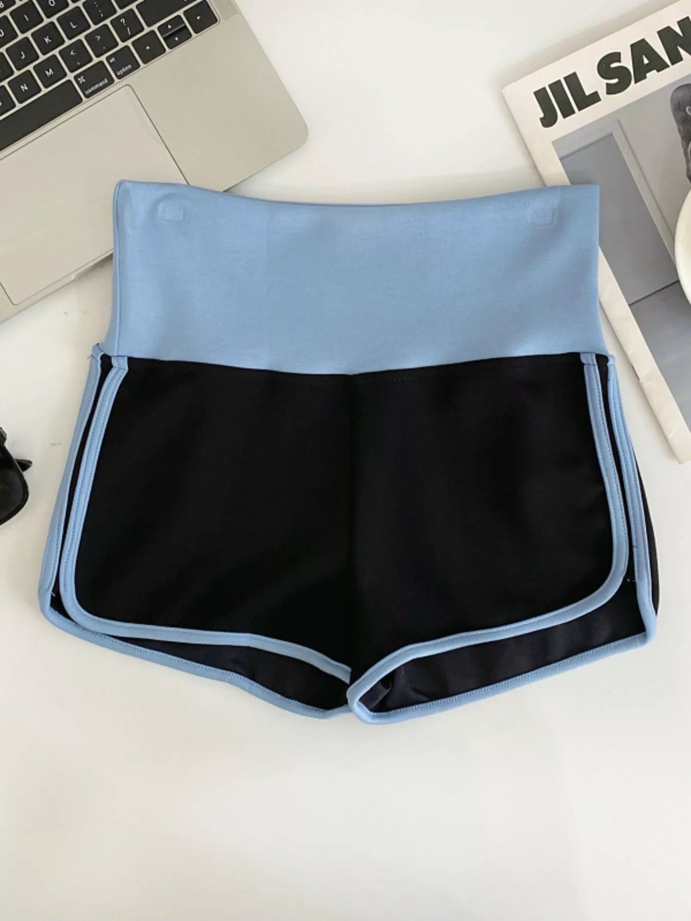 Black and blue shorts on a white surface with a laptop and magazine in the background.