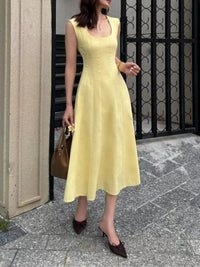 Woman in a yellow dress standing on a sidewalk with a black metal gate in the background.