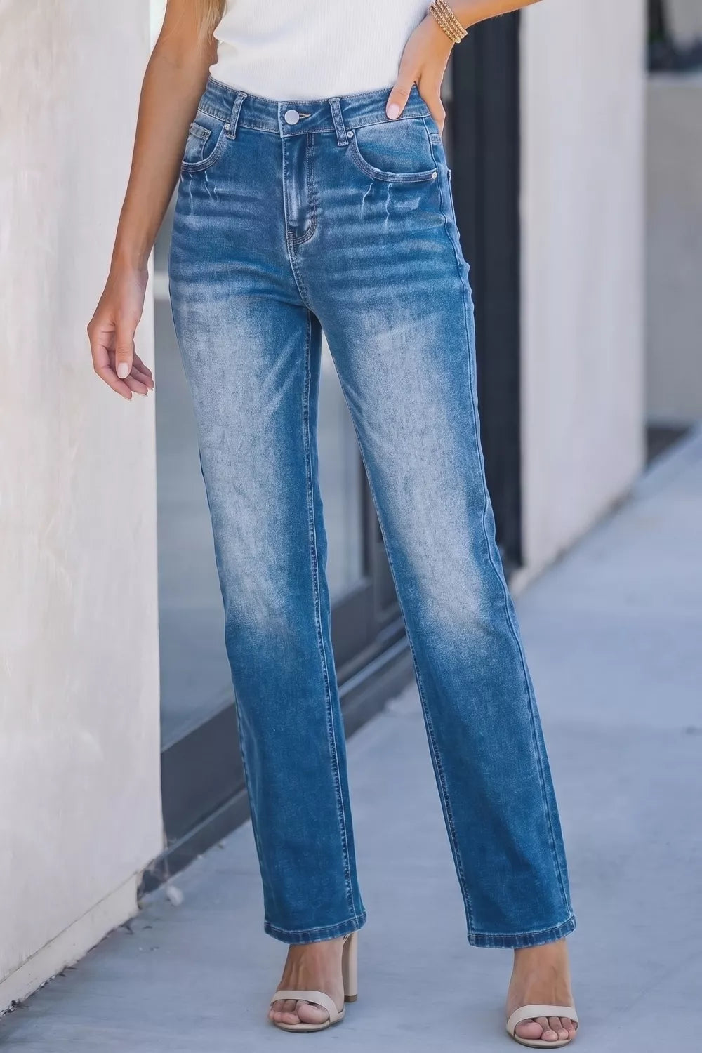 Person wearing blue jeans standing on a sidewalk.