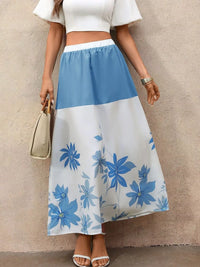 Person wearing a white top and blue floral skirt against a beige wall.