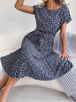 Woman wearing a navy blue floral dress sitting on a white couch.