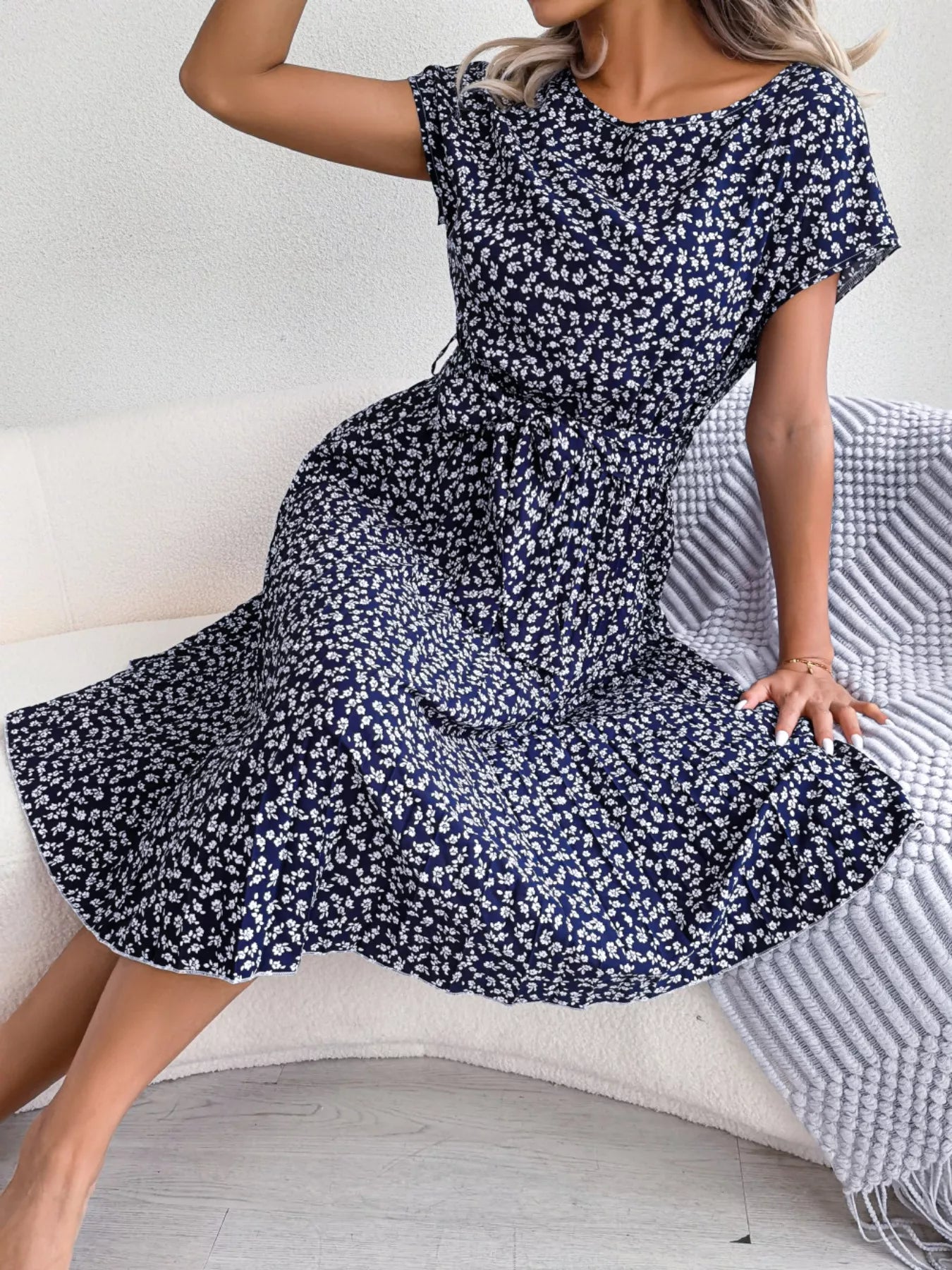 Woman wearing a navy blue floral dress sitting on a white couch.