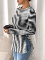 Person wearing a black and white striped sweater holding a coffee cup against a white curtain background