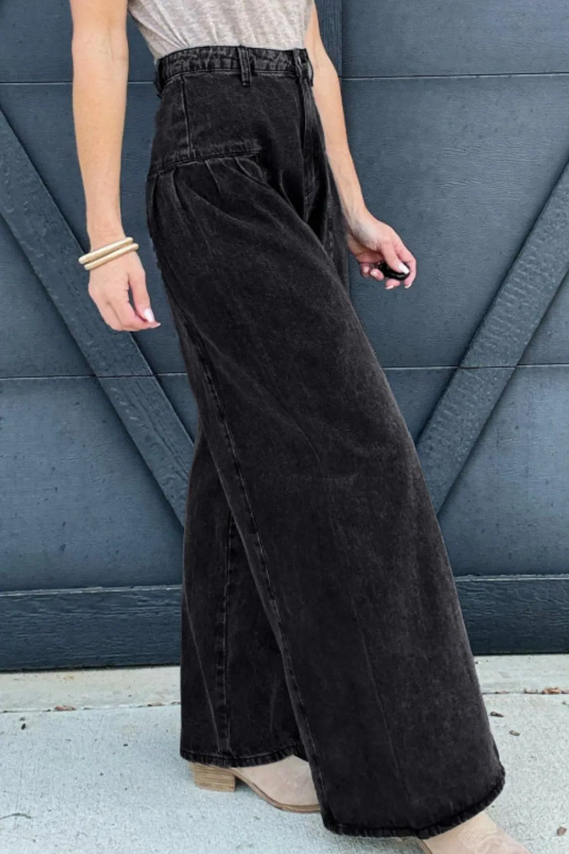 Person wearing black wide-leg jeans against a blue wall.