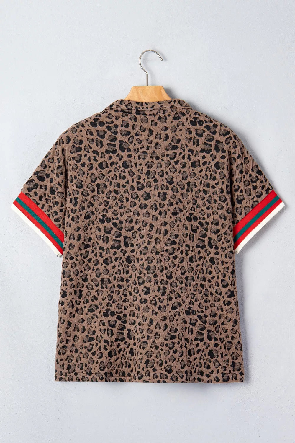 Leopard print shirt with red and green stripes on sleeves, hanging on a wooden hanger against a light gray background.