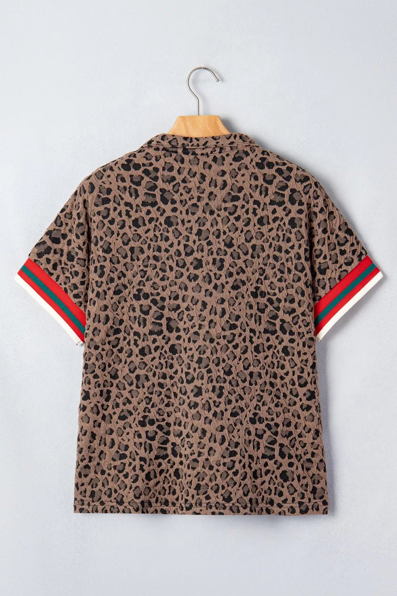 Leopard print shirt with red and green stripes on sleeves, hanging on a wooden hanger against a light gray background.