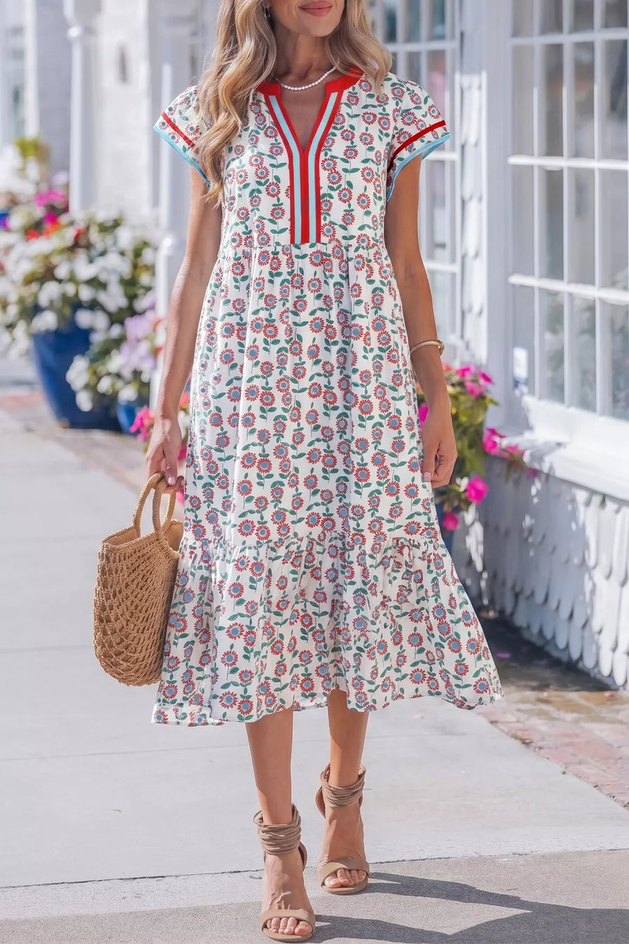 Woman wearing a floral dress with red accents, standing outdoors near flowers.
