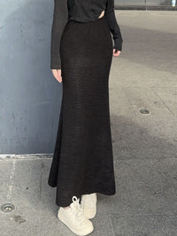Person wearing a black ribbed skirt and white sneakers on a gray pavement.