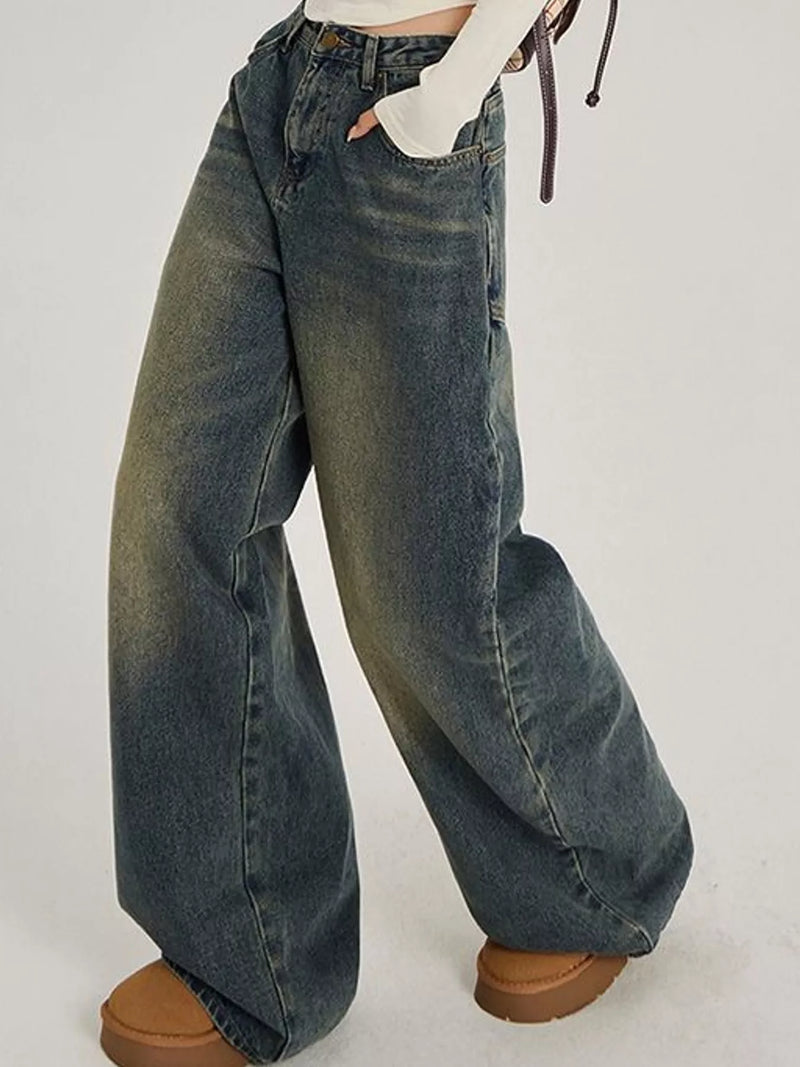 A person wearing very wide-leg faded blue denim jeans with a white cropped top and brown platform shoes, shown from the waist down against a plain light background.