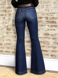 Blue jeans being worn against a brick wall.