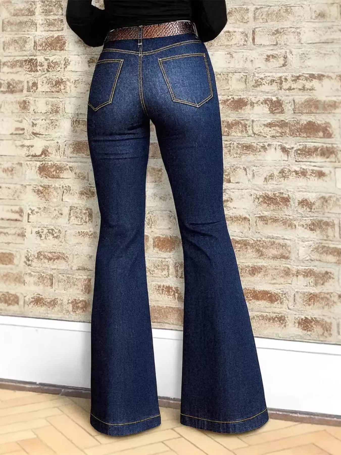 Blue jeans being worn against a brick wall.