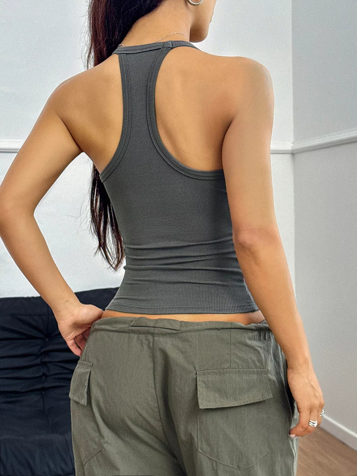 Person wearing a gray tank top and green cargo pants against a white wall.