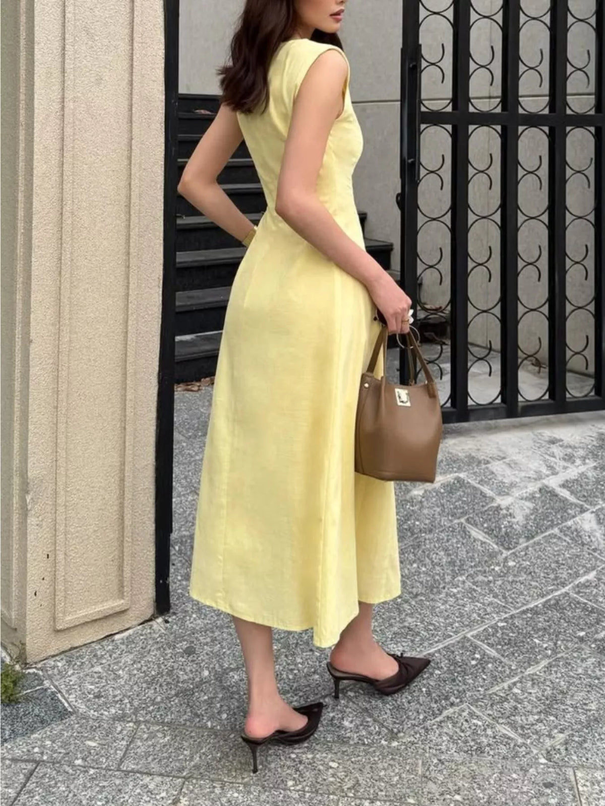 Woman in a yellow dress holding a brown handbag on a sidewalk.
