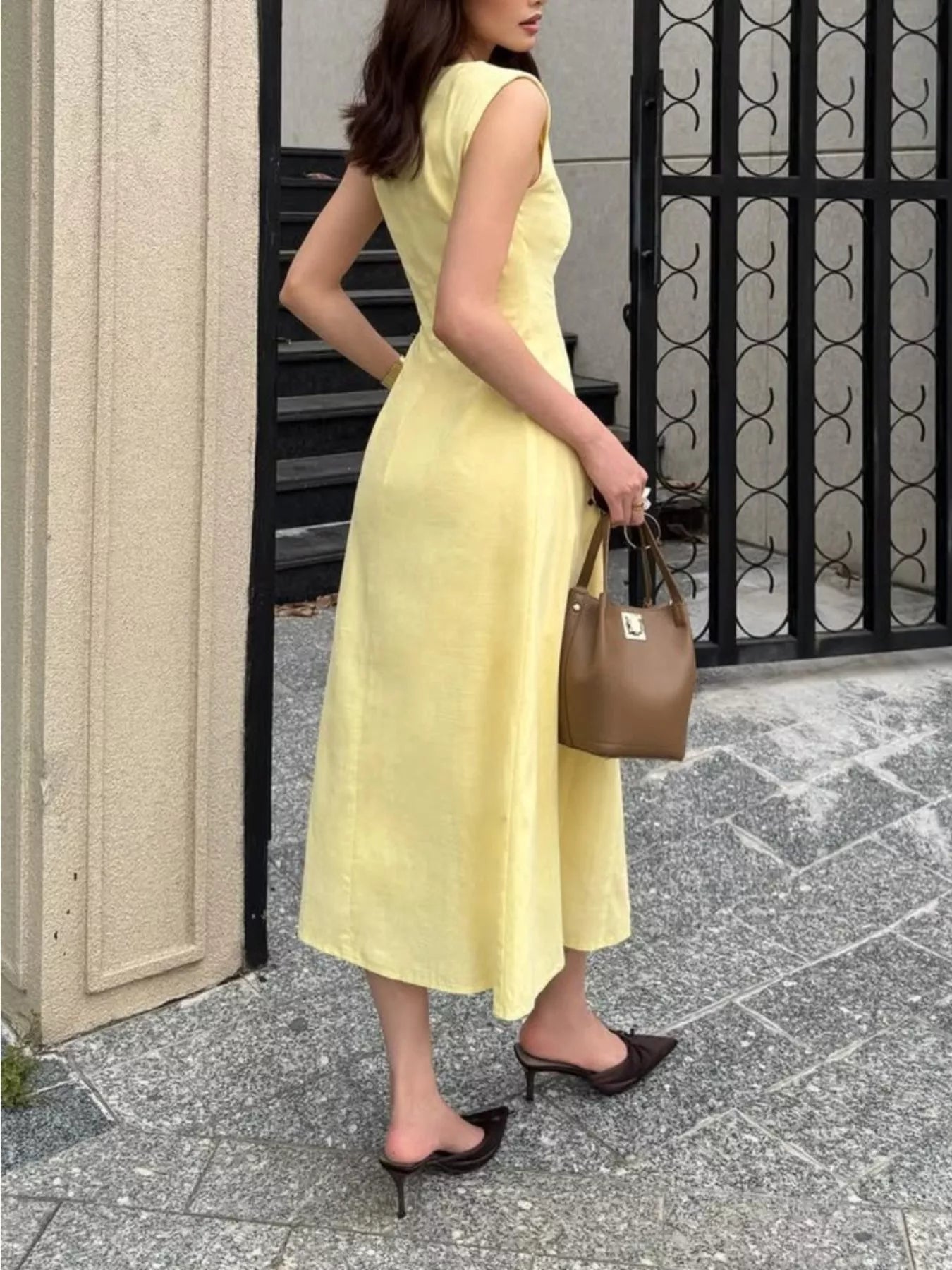 Woman in a yellow dress holding a brown handbag on a sidewalk.
