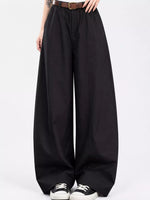 Black wide-leg trousers with a high waist, styled with a brown belt, black and white sneakers, and a visible model's hands and lower torso against a plain white studio background.