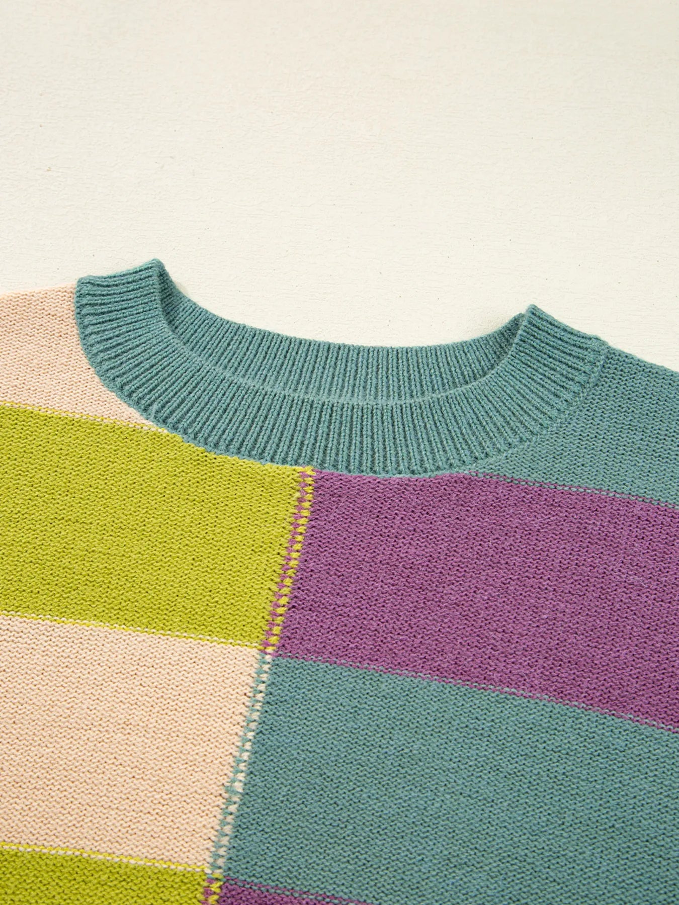 Color-blocked sweater with green, purple, and beige sections on a light background