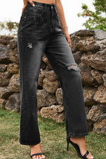 Person wearing black distressed jeans standing in front of a stone wall.