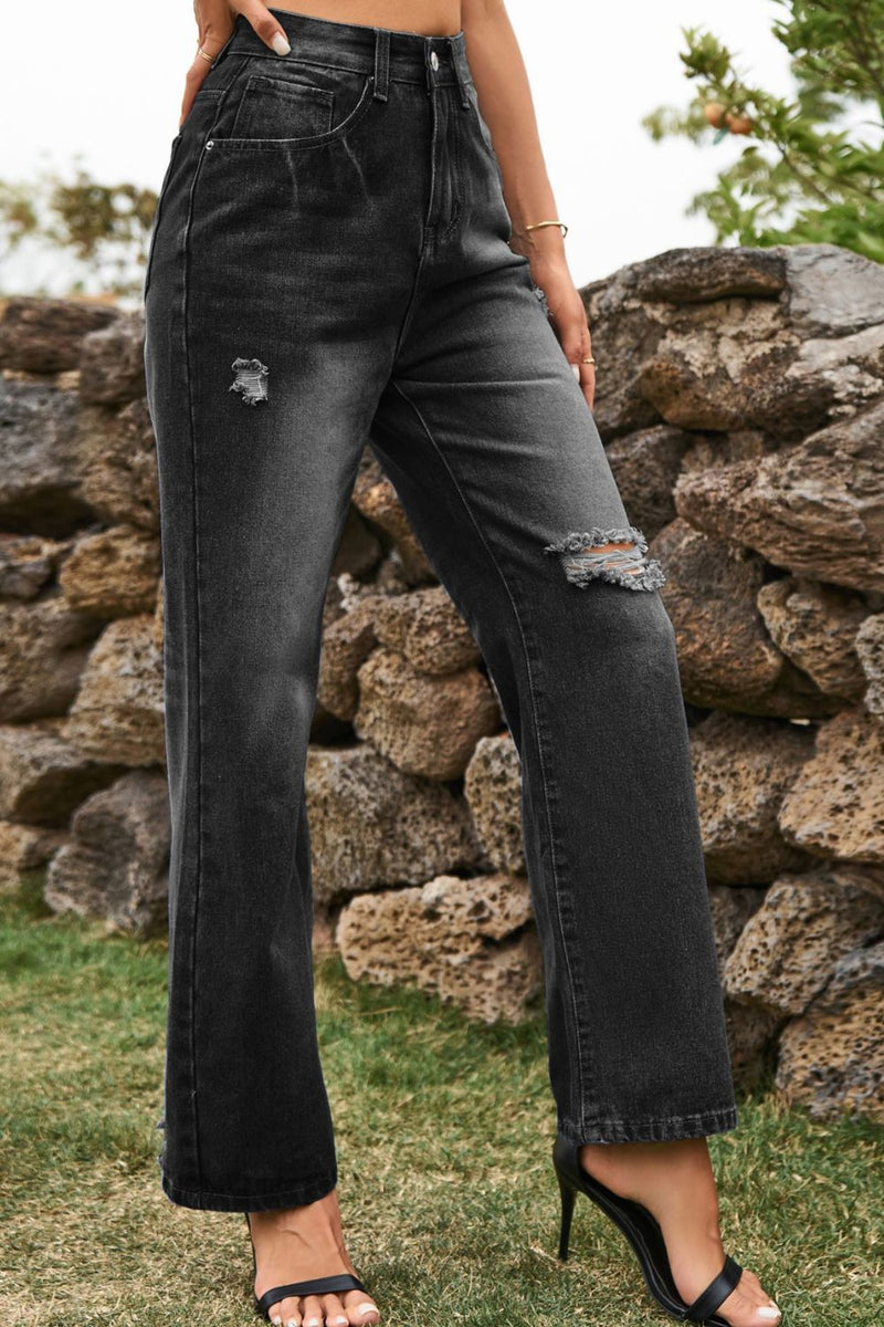 Person wearing black distressed jeans standing in front of a stone wall.