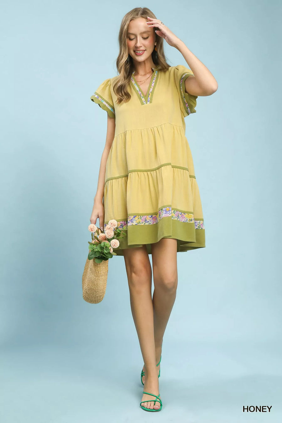 Woman wearing a yellow dress with floral details on a light blue background
