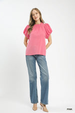 Woman wearing a pink blouse with puff sleeves and blue jeans on a white background