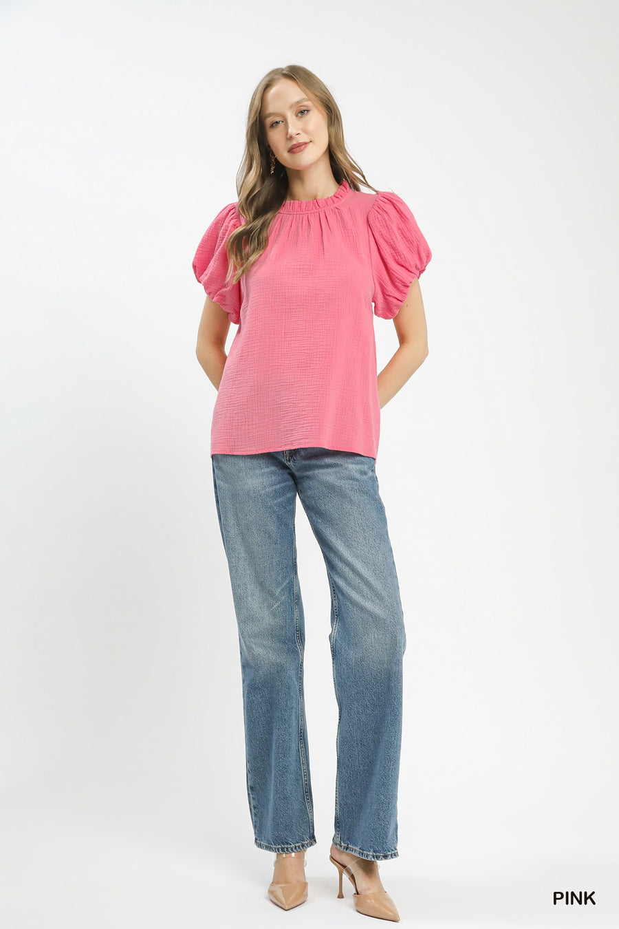 Woman wearing a pink blouse with puff sleeves and blue jeans on a white background
