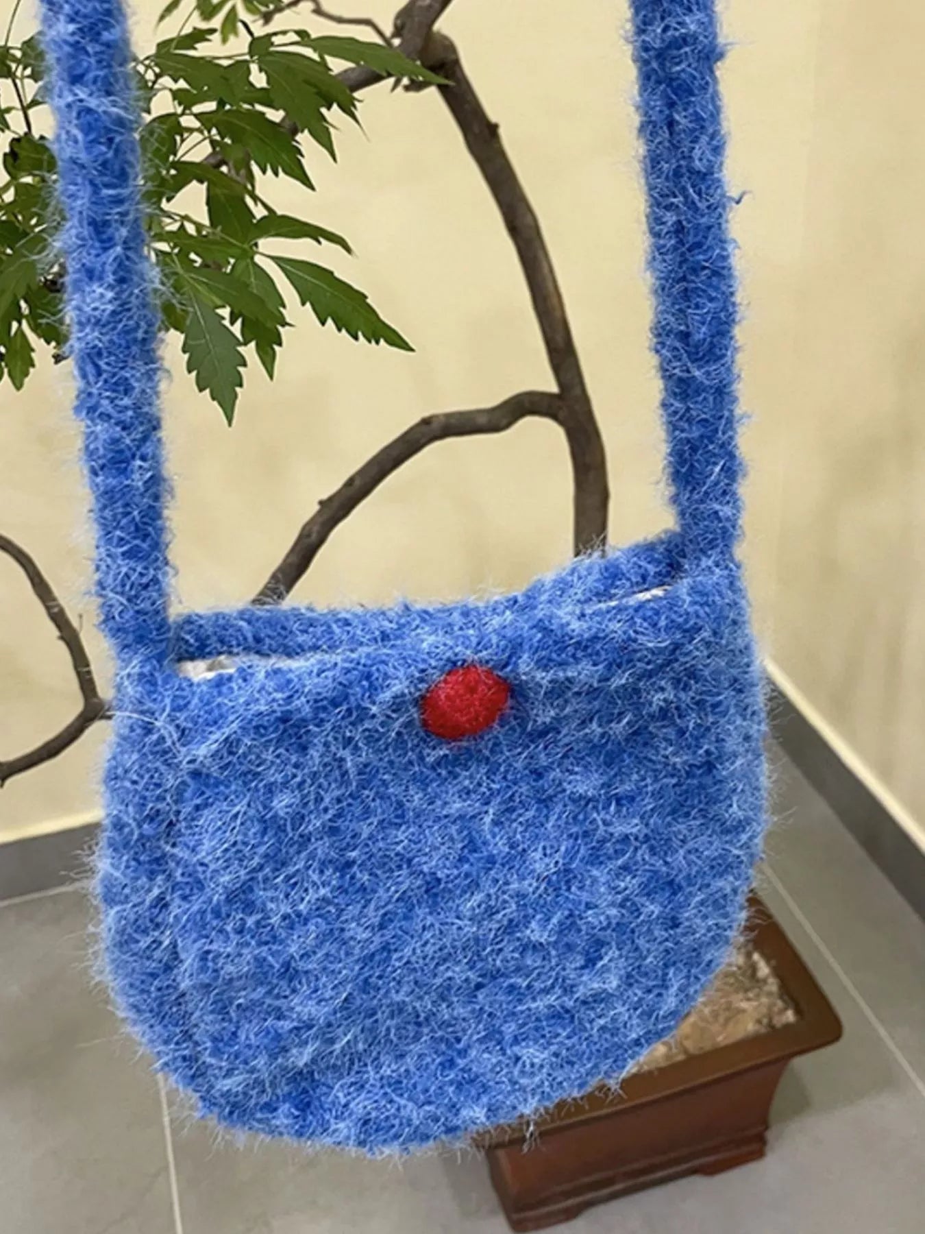 Blue textured handbag with a red button on a neutral background