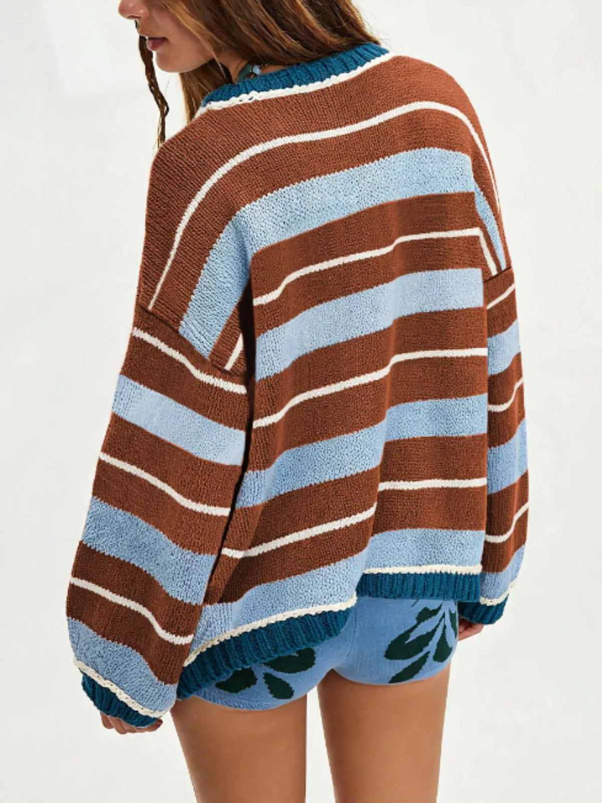 A woman wearing a loose, oversized knit sweater with horizontal brown, light blue, and white stripes, paired with matching blue shorts featuring a green leaf pattern, shown from a side-back angle against a plain white background.