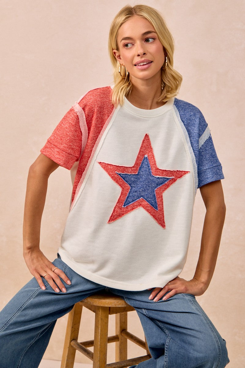 Woman wearing a white t-shirt with a red star design, sitting on a stool against a beige background.