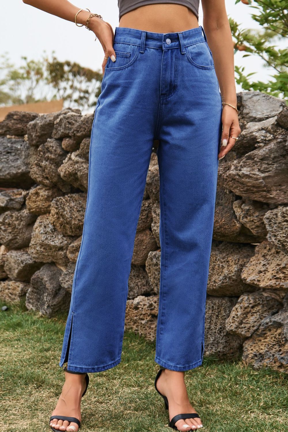 Person wearing blue jeans standing in front of a stone wall.