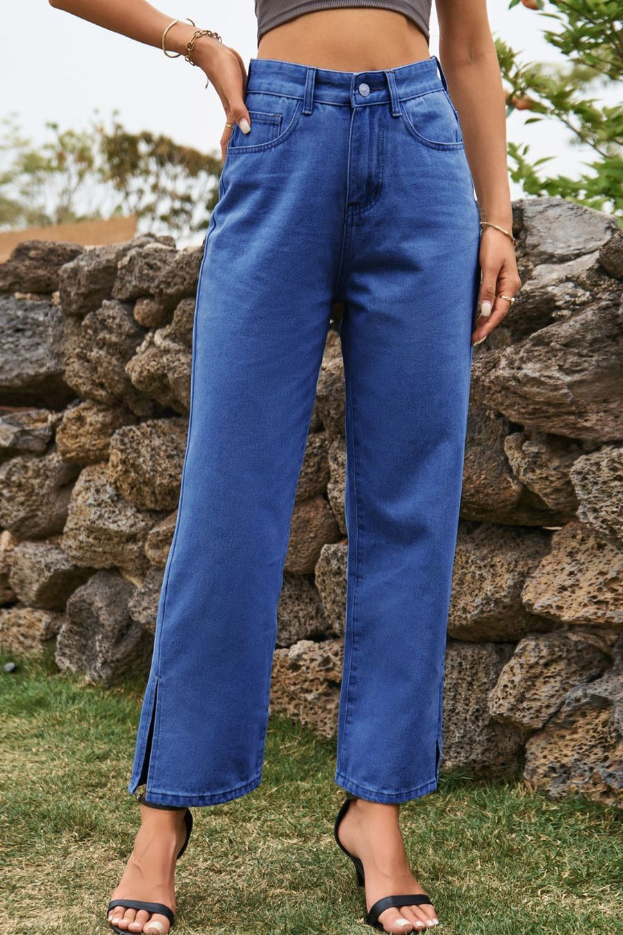 Person wearing blue jeans standing in front of a stone wall.