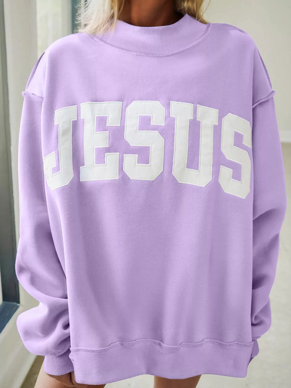 A person wearing an oversized light purple sweatshirt with the word 'JESUS' printed across the chest in large white varsity-style letters.