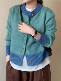 Person wearing a green and blue knitted cardigan with a plain background