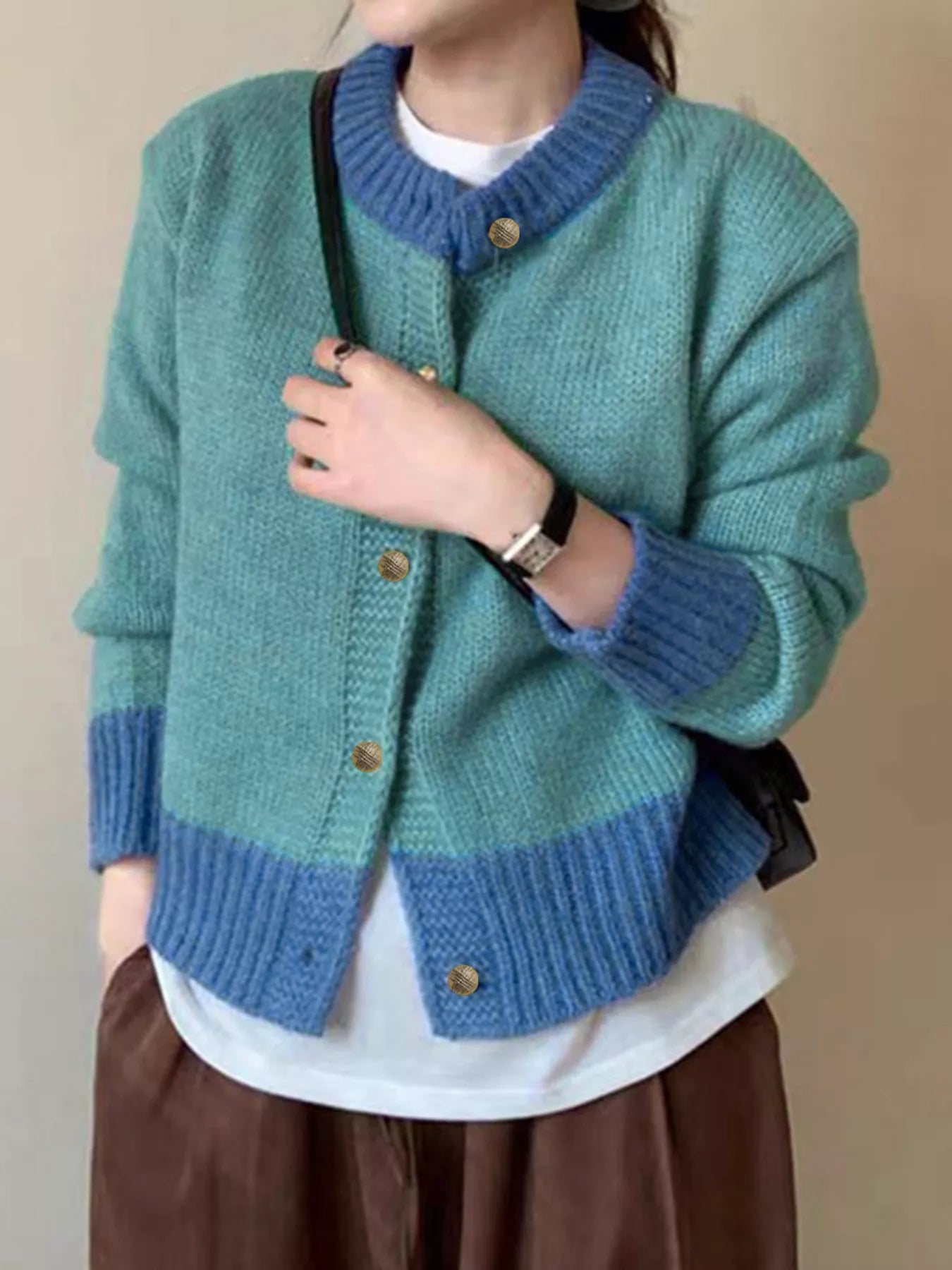 Person wearing a green and blue knitted cardigan with a plain background