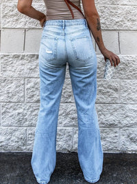 Person wearing light blue jeans standing against a stone wall.