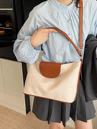 Person holding a beige and brown handbag in a kitchen setting
