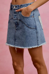 Blue denim skirt worn by a person on a pink background
